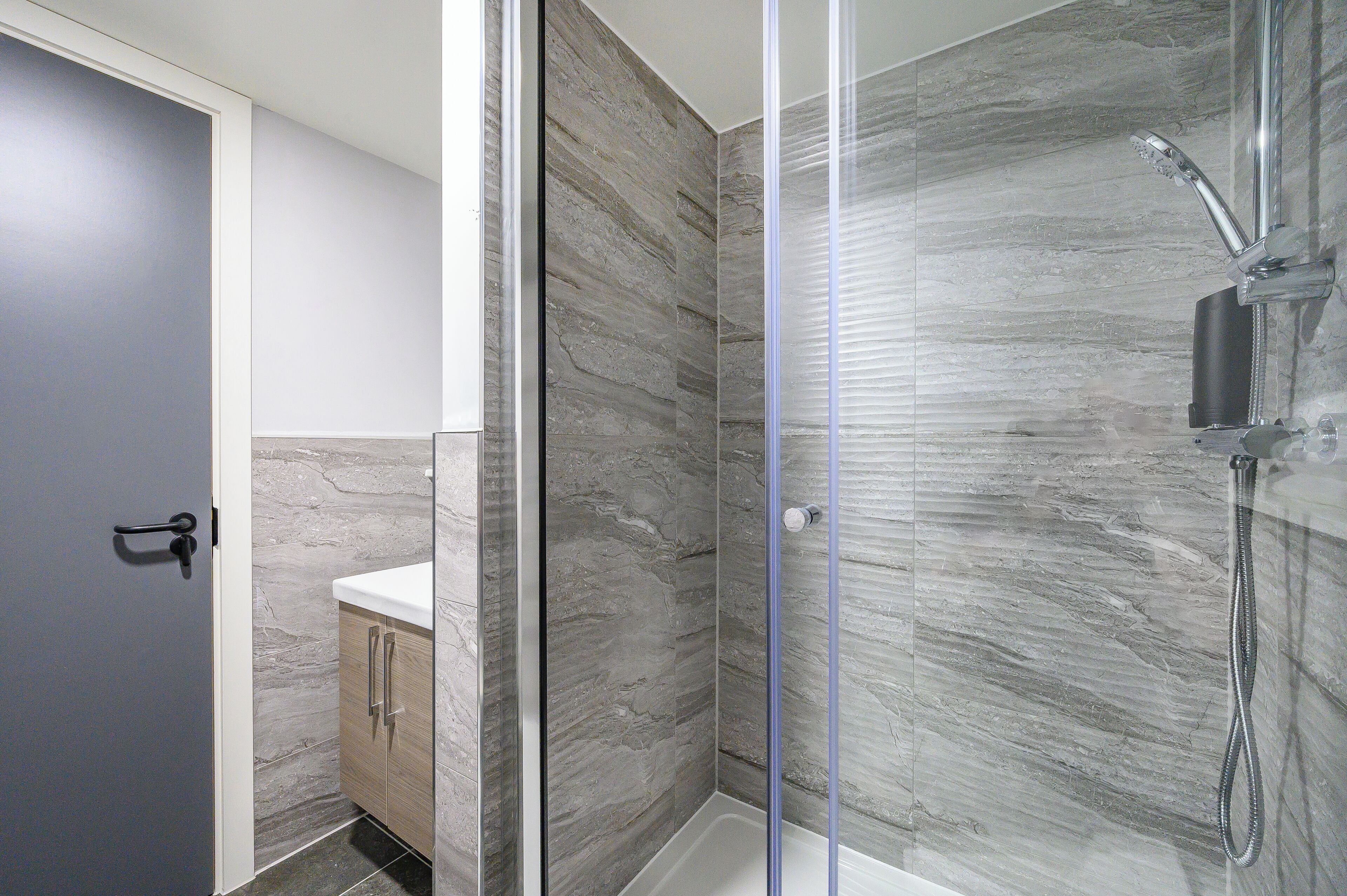 Une salle de bain moderne avec une douche à parois de verre, des murs en marbre et un meuble en bois.