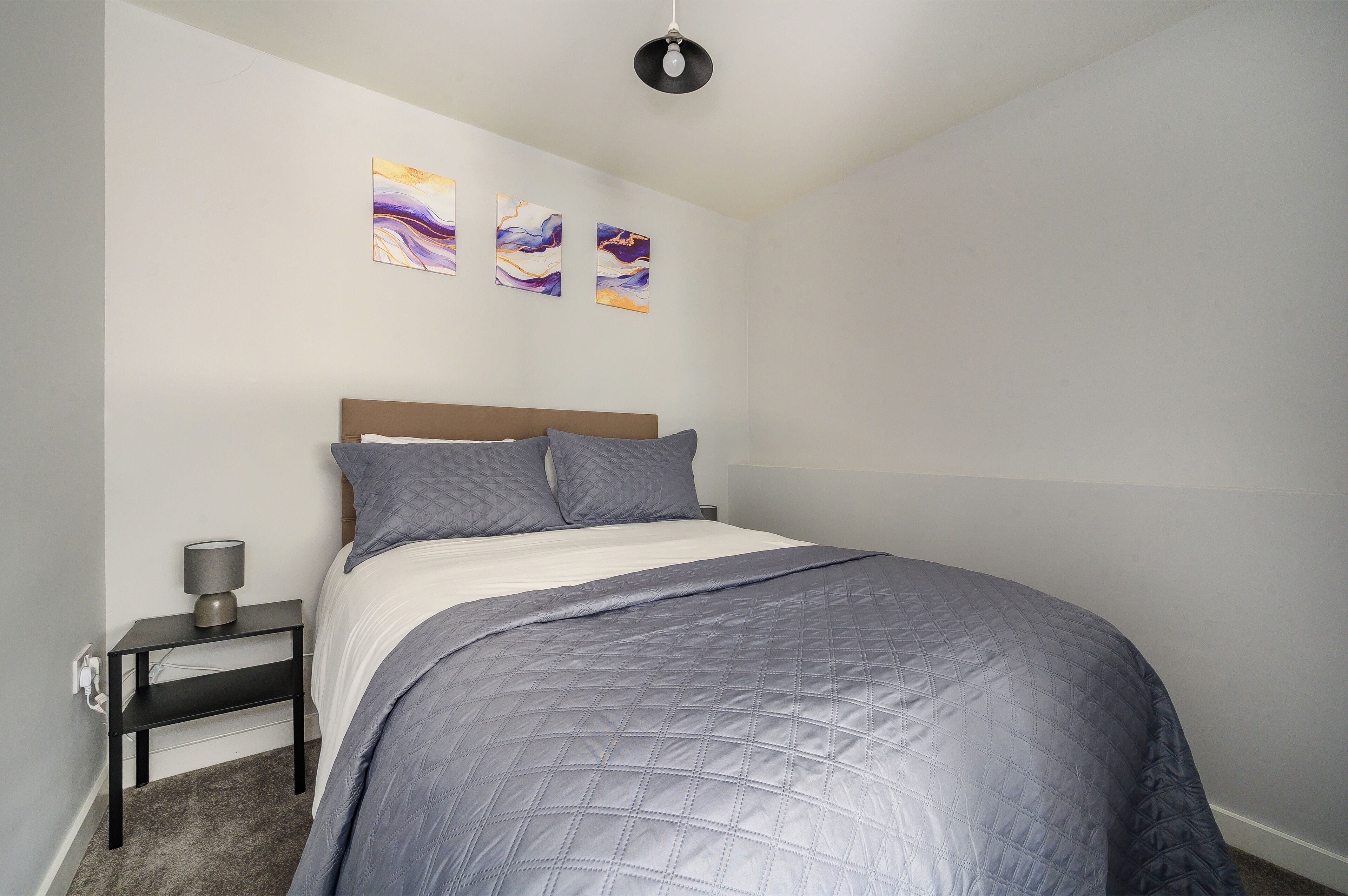 Une chambre à coucher avec un lit, une table de chevet et des œuvres d’art murales.