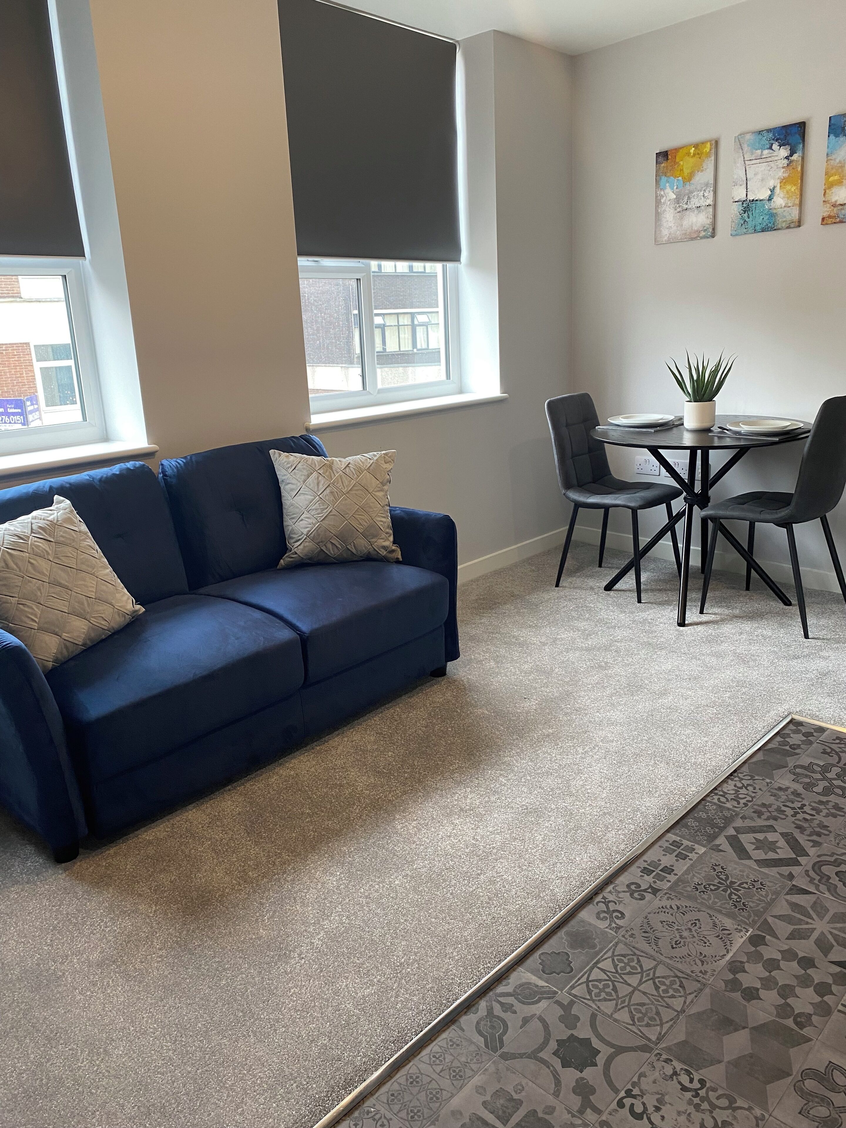 Un salon moderne avec un canapé bleu, une table à manger avec des chaises et une fenêtre avec des stores.