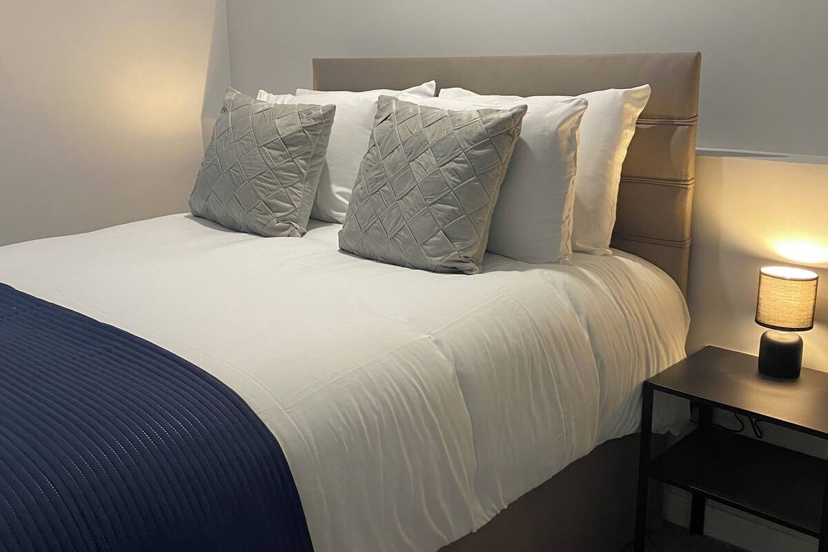 A neatly made bed with a blue blanket, a bedside lamp, and three abstract paintings on the wall.