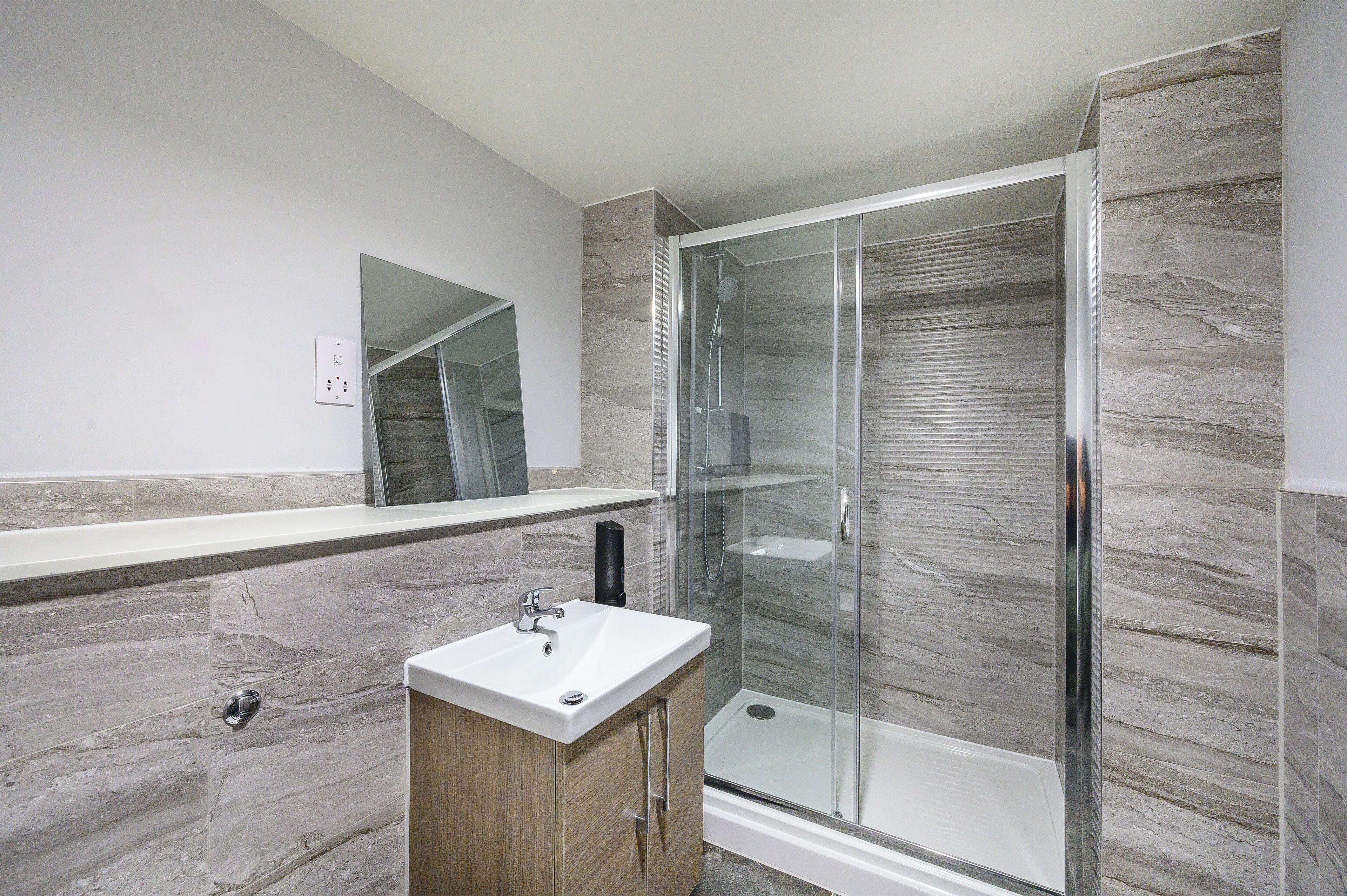 A modern bathroom with a glass-enclosed shower, a wooden vanity, and a marble backsplash.
