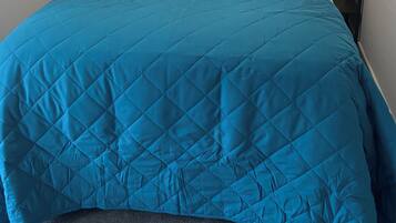 Una cama bien hecha con colcha azul, almohadas blancas y dos lámparas de noche.