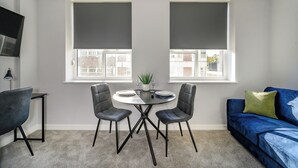 A modern living room with a round table and two chairs, a blue sofa, and a TV mounted on the wall. - Marygate by Deuce Hotels Ltd (Wakefield)