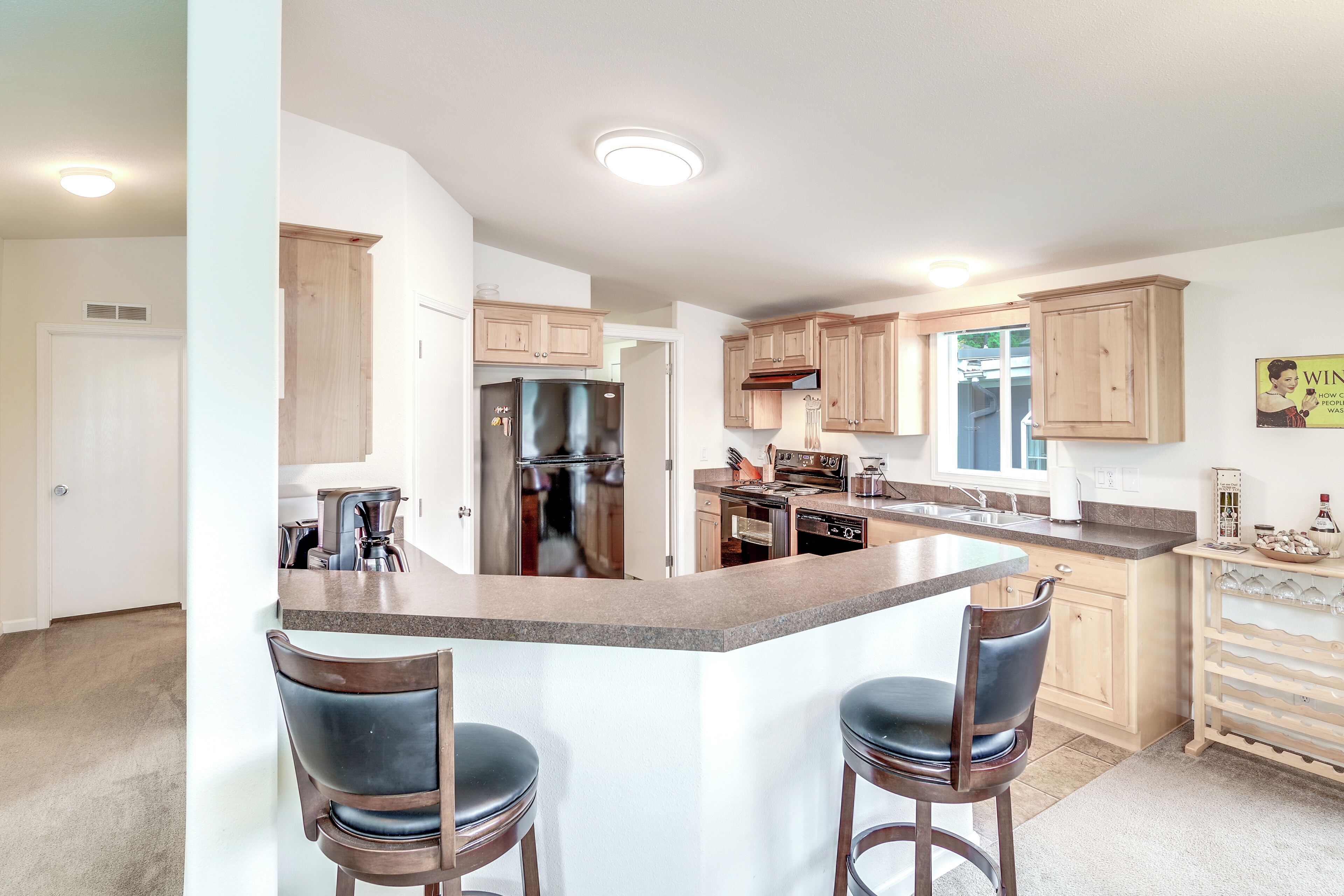 A modern kitchen with a central island, bar stools, wooden cabinets, and a built-in oven.