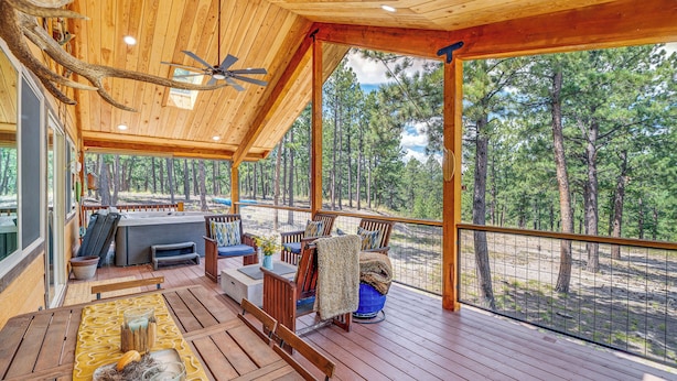Une terrasse en bois avec des sièges d’extérieur, un ventilateur de plafond et une vue sur une forêt.
