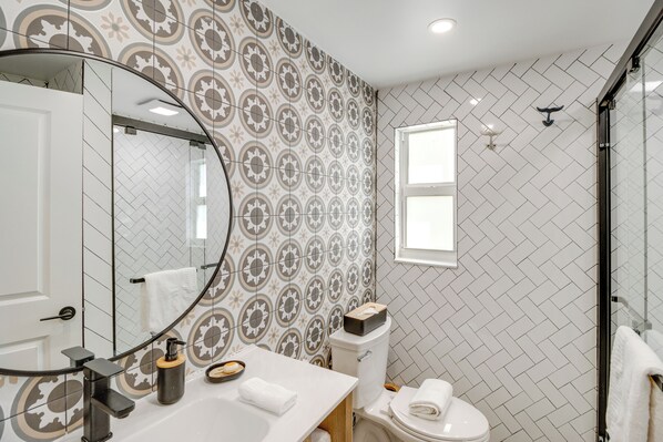 Une salle de bain avec un mur recouvert de carreaux à motifs, un lavabo blanc, un miroir et un espace douche.