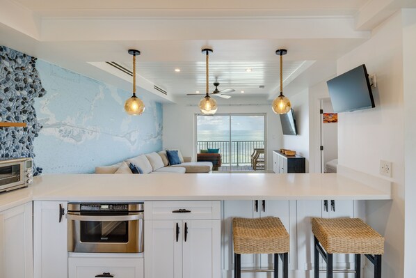 A modern kitchen with white cabinetry, a built-in oven, and a large island with stools. - Florida Keys Getaway w/ Stunning Ocean Views (Long Key)
