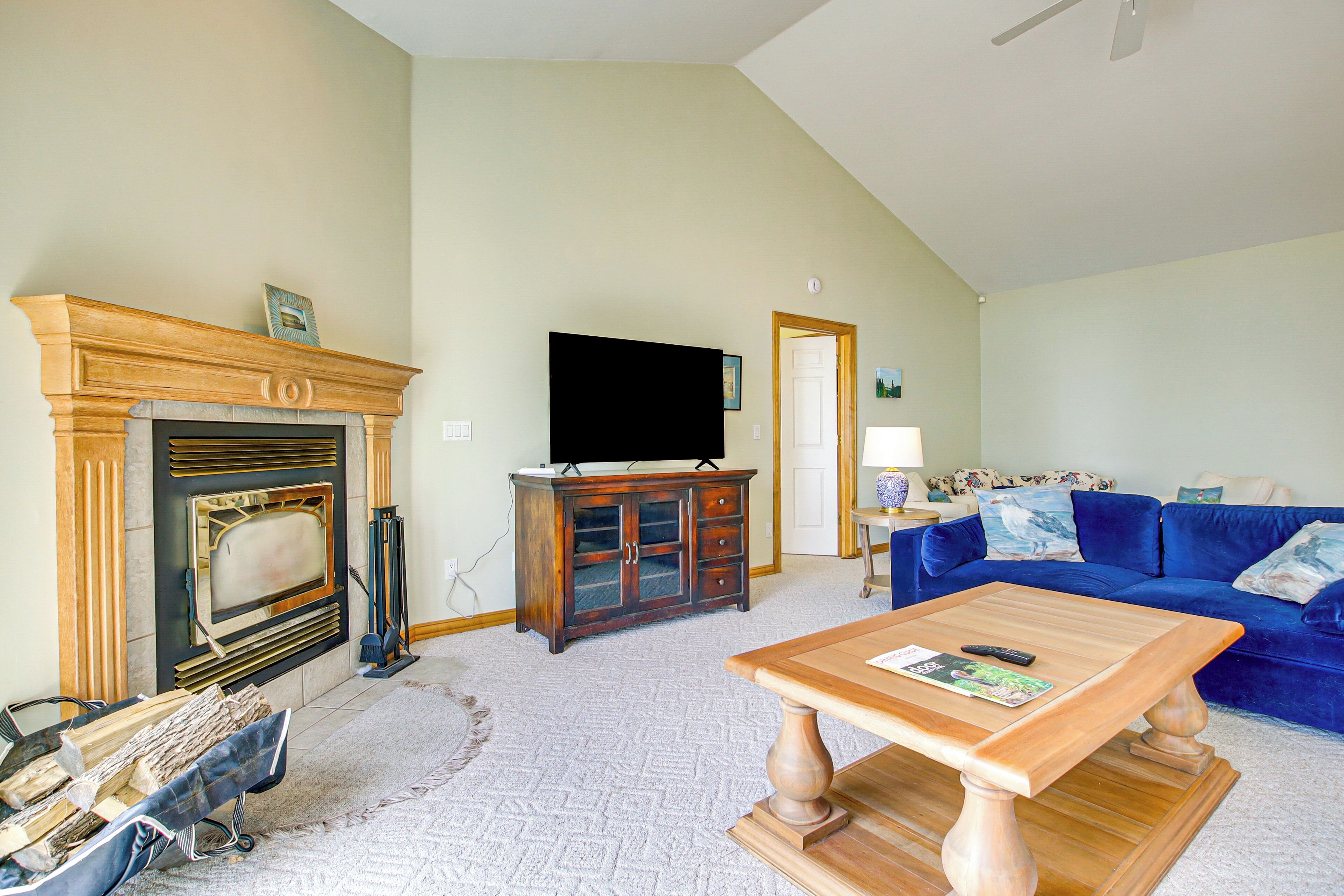 Una sala de estar con chimenea, un televisor sobre un mueble de madera, un sofá azul y una mesa de centro.