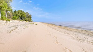 A sandy beach with footprints leading to the water, surrounded by trees.