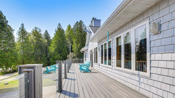 A wooden deck with two turquoise chairs and a table, overlooking a forested area.