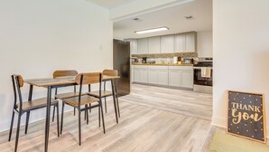 Una cocina moderna con armarios blancos, una mesa de comedor de madera con cuatro sillas y un cartel con la inscripción 'Thank You' en la pared.