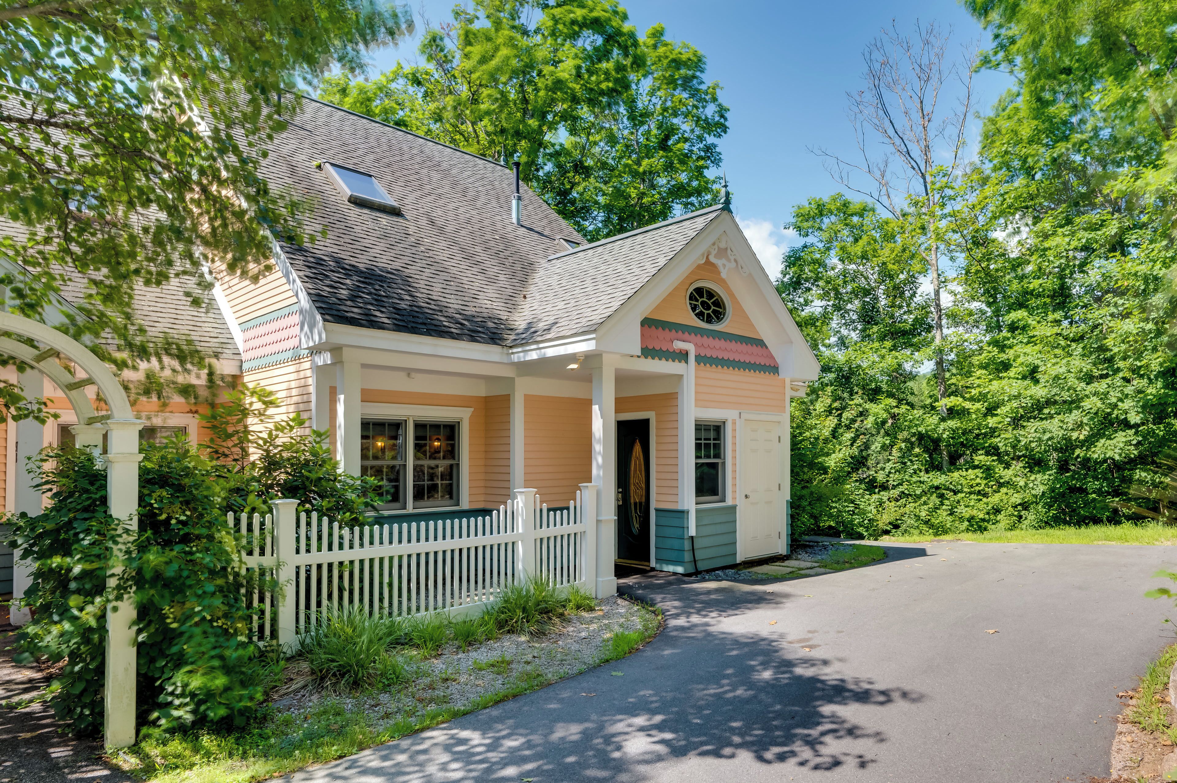 A two-story house with a porch, a picket fence, and a driveway leading to the entrance.