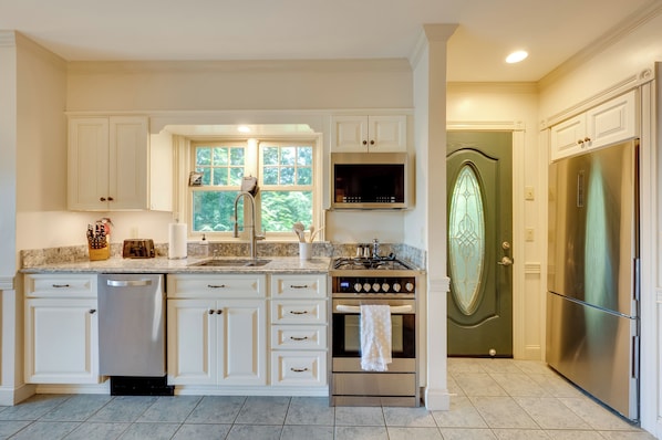 Una cocina con gabinetes blancos, lavavajillas de acero inoxidable, estufa y refrigerador.