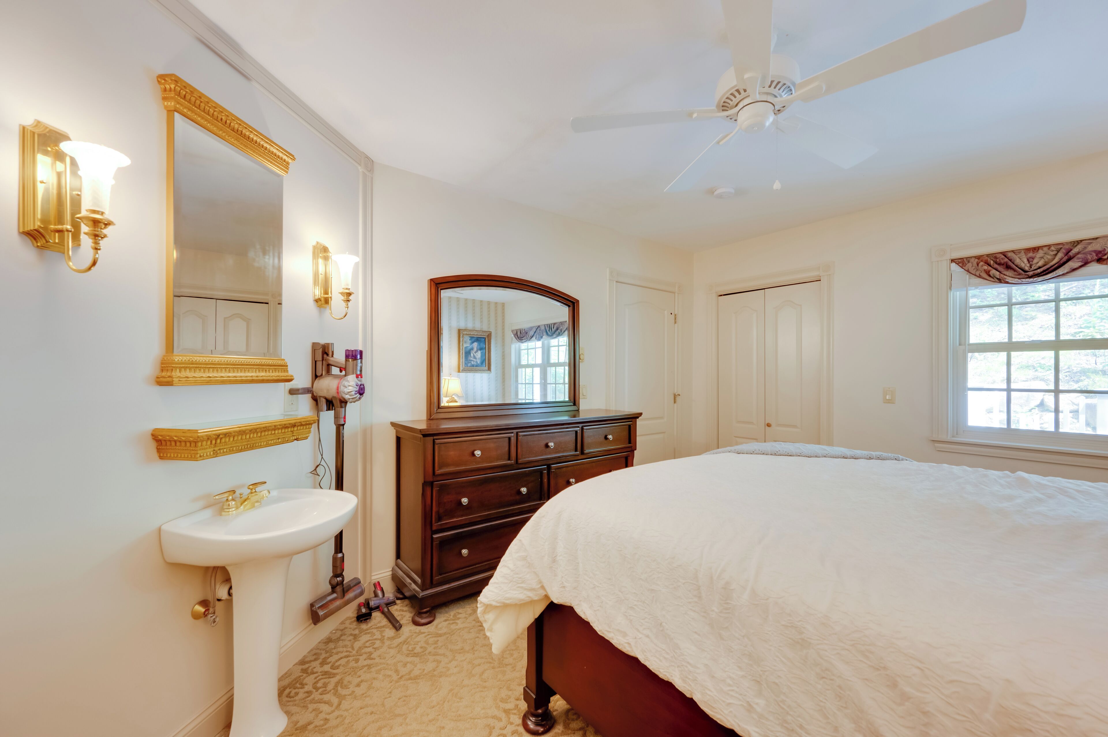 Un dormitorio con cama, cómoda, espejo, ventilador de techo y ventana.
