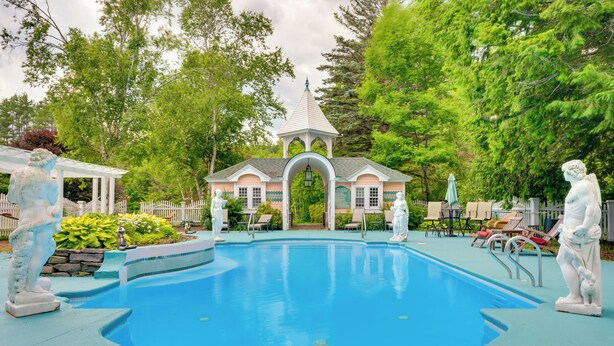 Ein Schwimmbad mit Gazebo, Statuen und einem weißen Zaun.