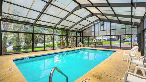 Una piscina interior con paredes de vidrio transparente, un indicador de profundidad de 90 centímetros y sillas de plástico blanco.