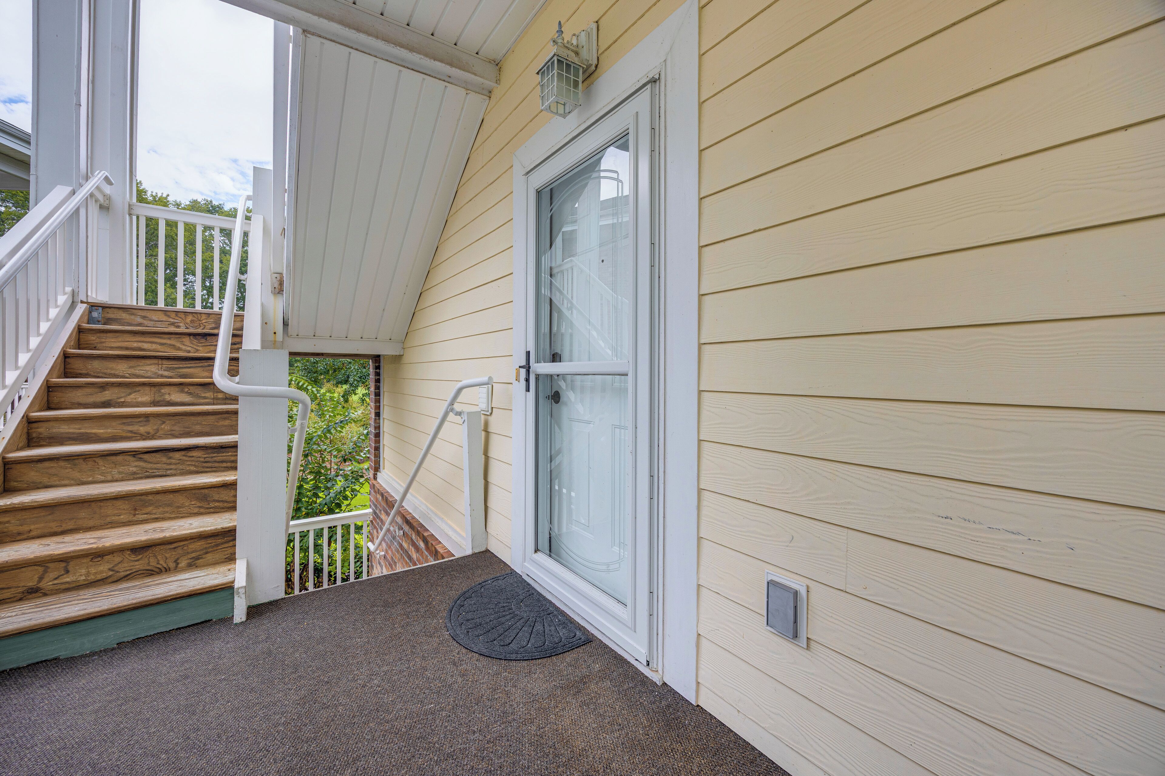 A wooden staircase leading to a porch with a glass door and a doormat.