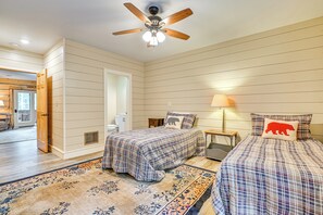 Une chambre avec deux lits, un ventilateur de plafond, une table de chevet et une lampe.