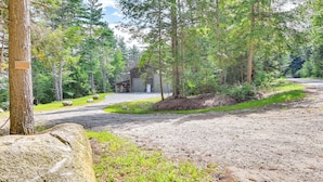 A rustic cabin surrounded by dense forest, with a gravel path leading to the entrance. - Tree Tops Retreat ~ 19 Mi to Lake George! (Chestertown)