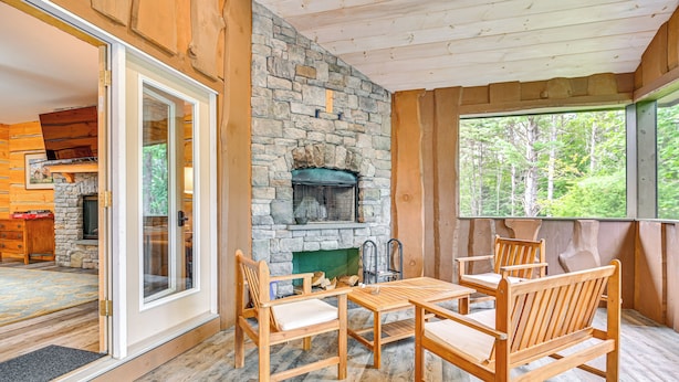 A wooden interior with a stone fireplace, wooden furniture, and a view of the outdoors. - Tree Tops Retreat ~ 19 Mi to Lake George! (Chestertown)