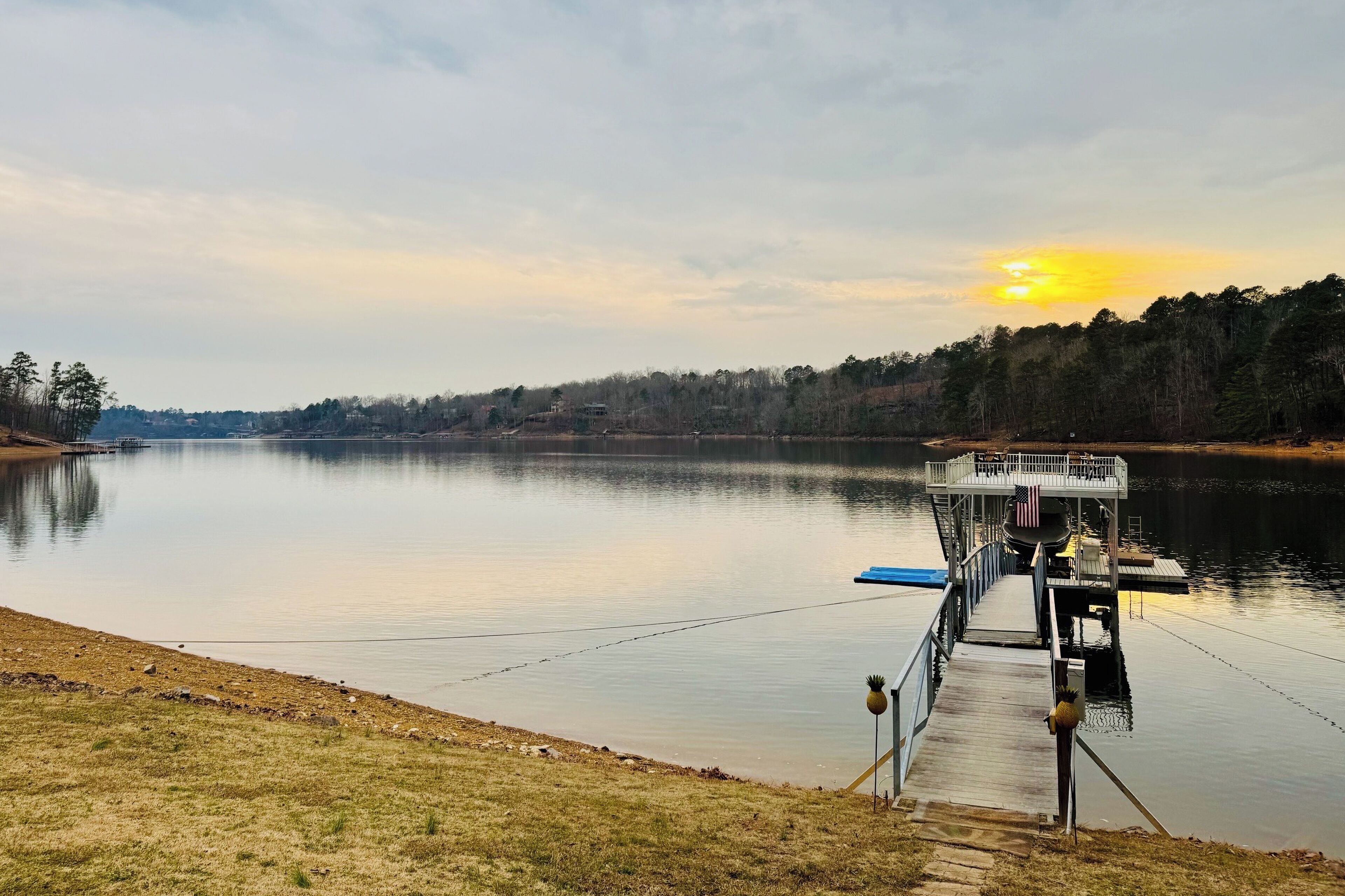 A calm lake with a dock extending into the water, surrounded by trees and a clear sky.