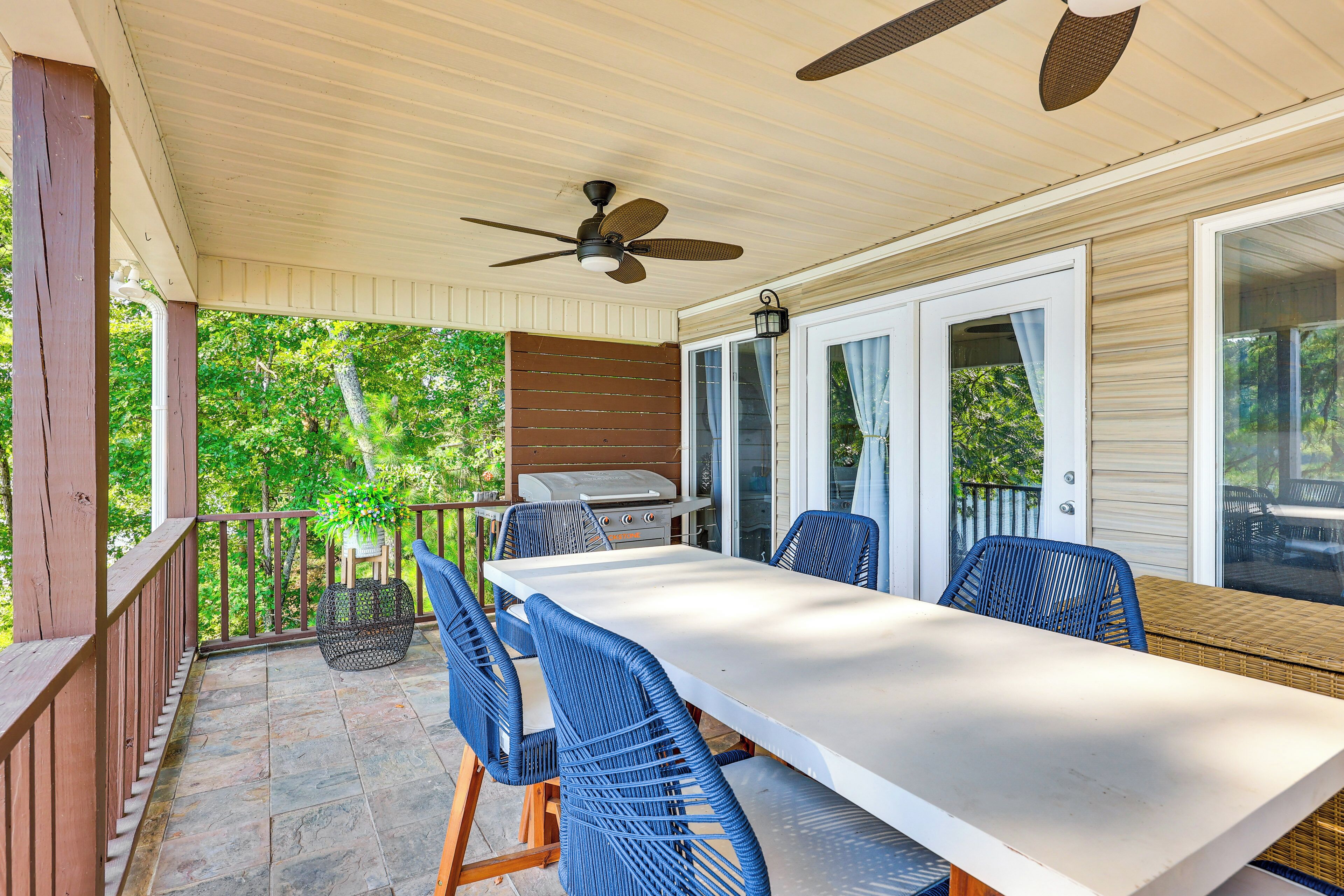 Une terrasse couverte avec une table et des chaises, un ventilateur de plafond et un barbecue.