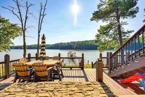 A wooden deck with a table and chairs overlooking a lake, a wooden staircase, and a view of the lake and trees. - Lewis Smith Lake Retreat w/ Dock & Deck! (Logan)