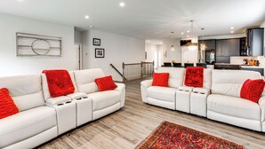 A modern living room with white sofas and red throw pillows, a wooden floor, and a kitchen in the background. - Home ~ 3 Mi to Penn State: Pets Welcome! (State College)