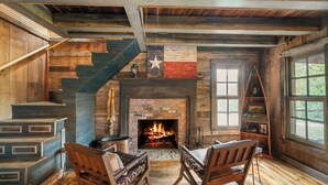 A rustic interior with a fireplace, wooden staircase, and a star flag. - Above Nashville Rustic Retreat Farm I 200 Acre Farm | Pool&Spa I Services (Charlotte)