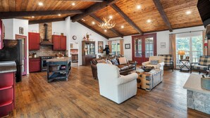 A spacious living area with a fireplace, wooden ceiling beams, and a large window offering a view of the outdoors. - Above Nashville Rustic Retreat Farm I 200 Acre Farm | Pool&Spa I Services (Charlotte)