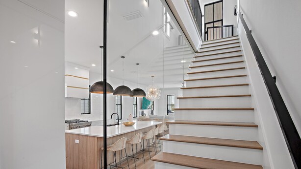 A modern kitchen with a central island, wooden stairs, and pendant lighting.