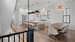 A modern kitchen with a central island, pendant lights, and a dining area with wicker chairs.