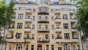 Un edificio de varios pisos con balcones, una entrada central y coches estacionados.