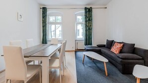 Una sala moderna con un sofá oscuro, una mesa de comedor de madera y sillas blancas.