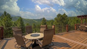 A wooden deck with a round table and chairs, surrounded by a metal railing, overlooking a mountainous landscape. - Aspen Valley, Deadwood SD (Sturgis)