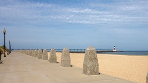 Un paseo marítimo con bolardos de piedra, un muelle y un faro a lo lejos.