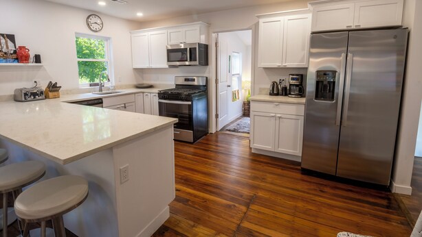 Una cocina moderna con armarios blancos, electrodomésticos de acero inoxidable, una isla grande con taburetes y piso de madera.