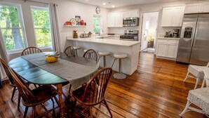Una cocina moderna con armarios blancos, electrodomésticos de acero inoxidable y una mesa de comedor de madera con sillas.