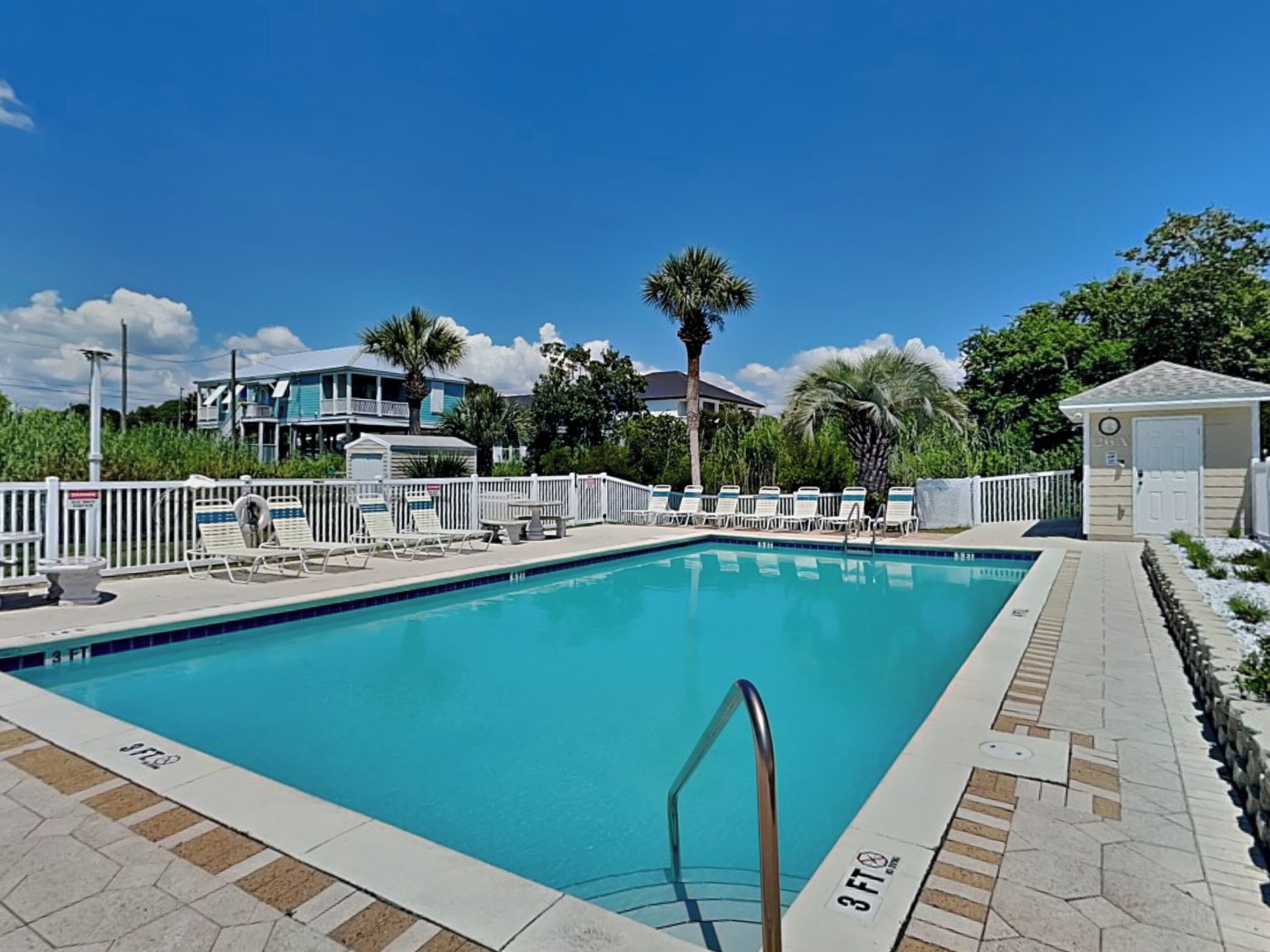 A rectangular swimming pool with a 3 ft depth marker, surrounded by a white fence, with a clear blue sky above.