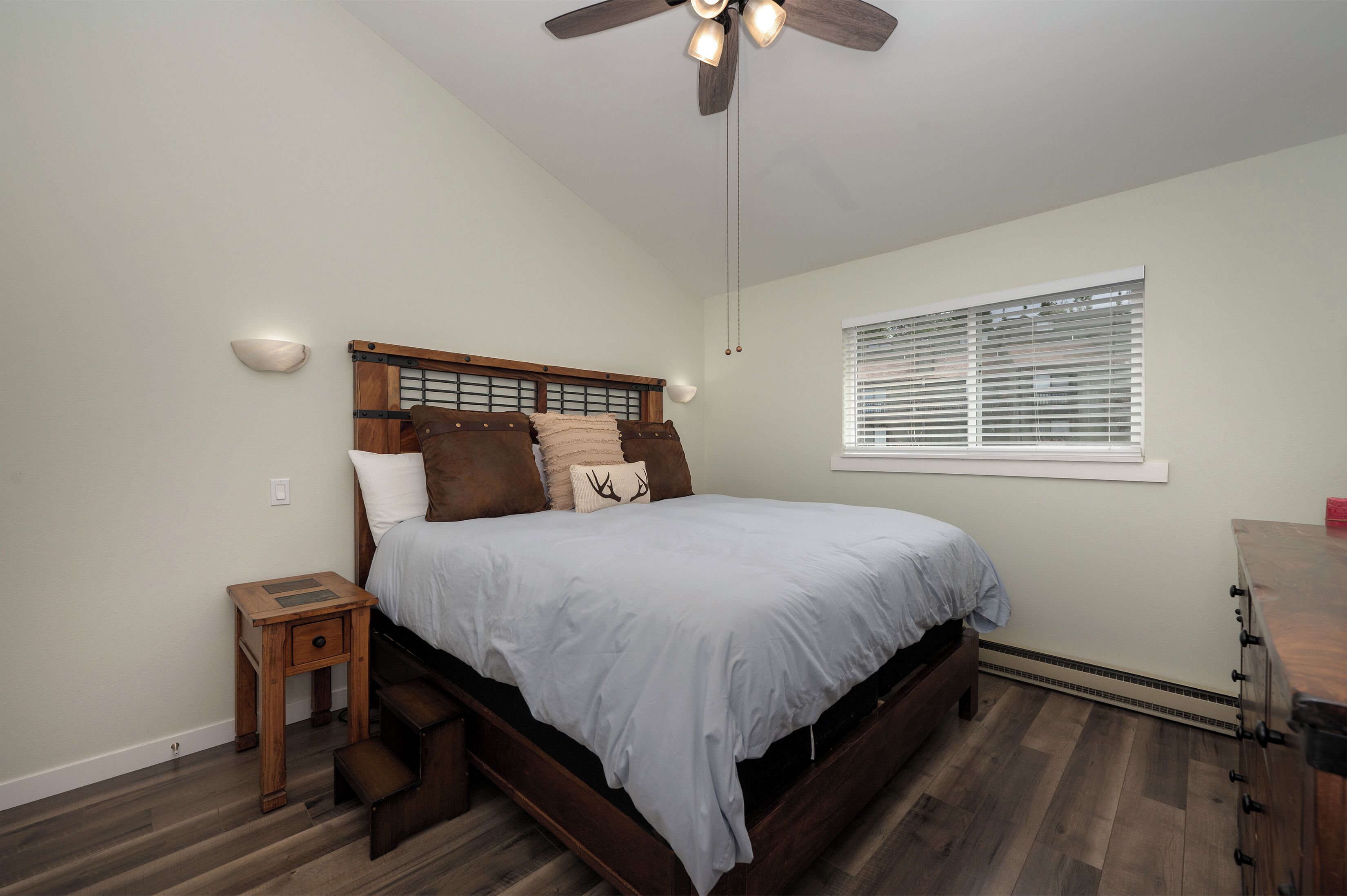 A bedroom with a bed, a nightstand, a ceiling fan, a window with blinds, and a dresser.