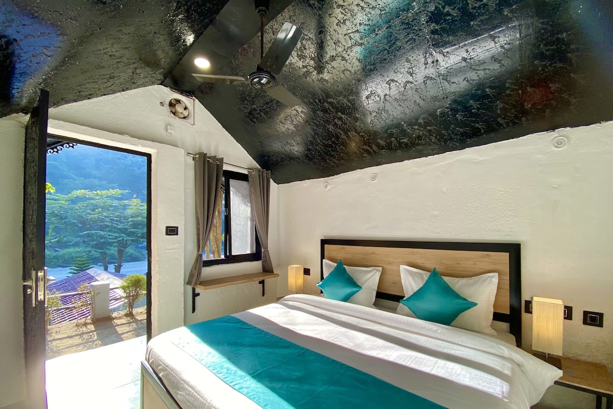 A bedroom with a bed, a ceiling fan, a window with curtains, and a view of greenery outside.