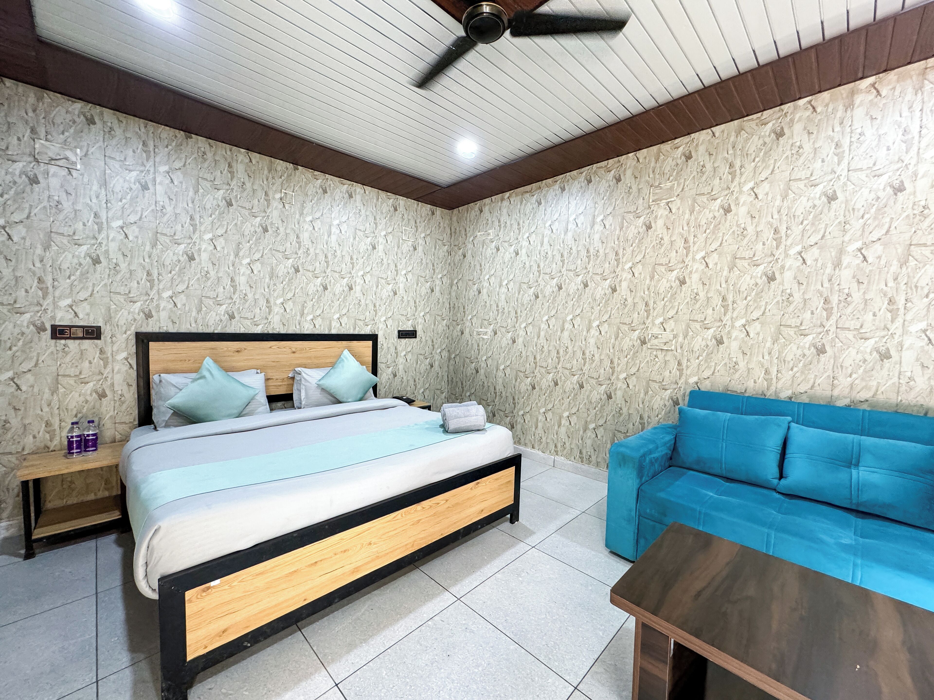 A bedroom with a bed, a blue sofa, a wooden nightstand, and a ceiling fan.