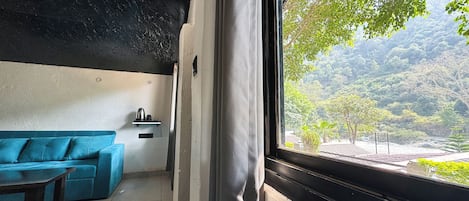 Una habitación con un sofá azul, una mesita y una ventana que da a una zona boscosa.