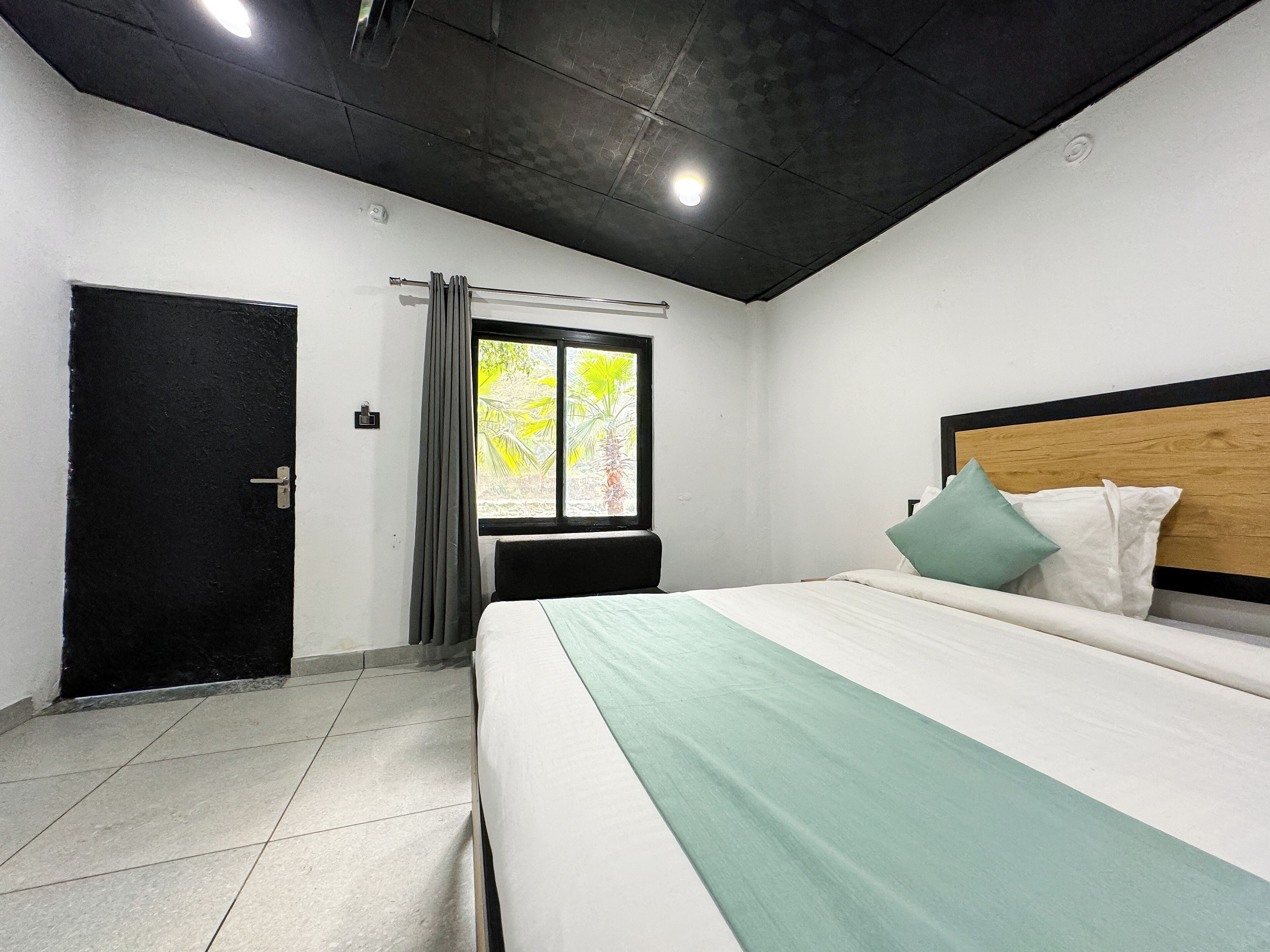 A bedroom with a bed, a window with curtains, a door, and a ceiling light.