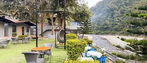 A hotel patio with outdoor seating, a hanging chair, and a view of a river.