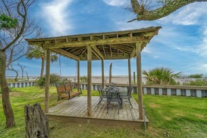 Un belvédère en bois, équipé d’une balançoire et de chaises en métal, qui offre une vue sur la plage.
