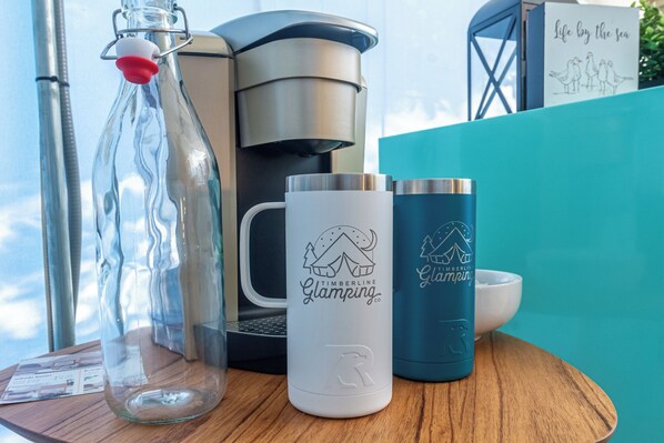 Una mesa de madera con una botella de vidrio, una taza blanca y una taza azul con el logo de un oso.