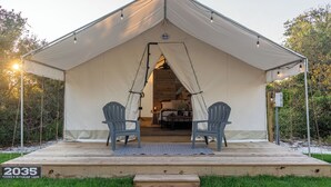 A large tented accommodation with two chairs on a wooden deck, a sign indicating '2035 Young's Hideaway Lane', and a view of the interior with a bed and a table.