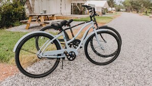 Una bicicleta estacionada en un camino de grava con una mesa de picnic y un edificio blanco al fondo.