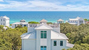 A coastal property with multiple buildings, including a prominent white house with a green window, surrounded by lush greenery and overlooking the ocean. - Barefoot By The Sea|Easy Beach Access|Private Pool|Gulf Views from Lookout Tower (Santa Rosa Beach)
